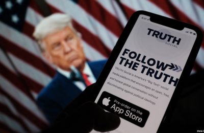 Seseorang sedang melihat aplikasi "Truth Social" di ponsel, dengan foto mantan presiden AS Donald Trump sebagai latar belakang, di Los Angeles, 20 Oktober 2021. (Foto: AFP/ Chris Delmas)