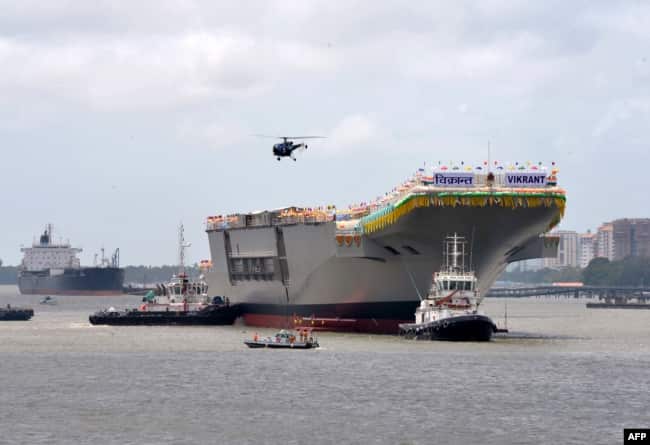 Kapal tunda memandu kapal induk buatan dalam negeri INS Vikrant saat meninggalkan dermaga Cochin Shipyard Limited setelah diluncurkan di Kochi. (Foto: AFP)