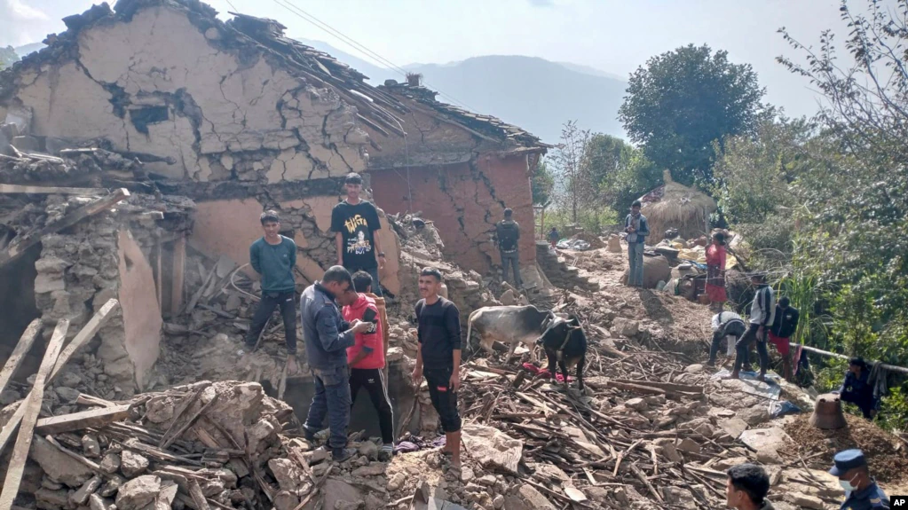 Penduduk desa Nepal berdiri di antara puing-puing rumah lumpur mereka setelah gempa bumi di distrik Doti, Nepal, Rabu, 9 November 2022. (Foto: AP)