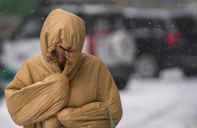 Seorang perempuan menggunakan pakaian musim dinginnya untuk melindungi badannya dari angin dan salju yang muncul di jalanan kota Beijing saat ibu kota China itu dilanda oleh badai salju pada 7 November 2021. (Foto: AP/Andy Wong)