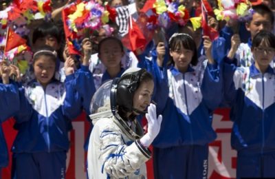 Pelajar China melambaikan bunga dan bendera nasional saat astronot perempuan Wang Yaping meninggalkan pusat peluncuran satelit Jiuquan menuju lokasi peluncuran, dekat Jiuquan, China barat, Selasa, 11 Juni 2013. (Foto: AP/Andy Wong)