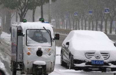 Seorang petugas pengantaran dengan motornya bergerak melewati mobil yang berselimut salju di di Beijing, China, pada 7 November 2021. (Foto: AP/Ng Han Guan)