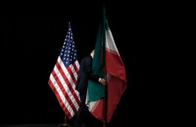 Seorang petugas membereskan bendera Iran yang terpasang di samping bendera AS dari atas panggung setelah pembicaraan nuklir Iran selesai dilaksanakan di Wina, Austria, pada 14 Juli 2015. (AP/Carlos Barria)