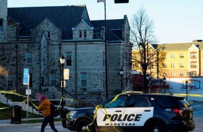 Seorang warga tampak berjalan melewati mobil polisi yang memblokade jalan utama di Kota Waukesha, Wisconsin, pada 22 November 2021, sehari setelah insiden penabrakan terhadap rombongan parade natal terjadi di kota tersebut. (Foto: Reuters/Cheney Orr)