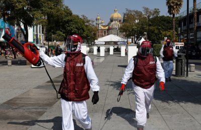 Para petugas menyemprotkan desinfektan di sekitar Basilika Guadalupe di barat daya Mexico City, Meksiko yang ramai dikunjungi wisatawan menjelang 12 Desember (foto: dok).