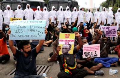 Polisi mengenakan APD berbaris di dekat aktivis Papua yang berunjuk rasa di luar Kompleks Monumen Nasional di Jakarta, Indonesia, 1 Desember 2021. (REUTERS/Willy Kurniawan).