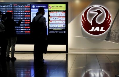 Pria berdiri di samping logo Japan Airlines (JAL), di tengah wabah COVID-19, di Bandara Internasional Tokyo, yang biasa disebut Bandara Haneda di Tokyo, Jepang, 30 Oktober 2020. (Foto: REUTERS/Issei Kato)