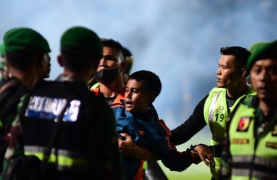 Seorang anak laki-laki (tengah) digendong oleh anggota TNI yang berusaha mengamankan satdion ketika kisruh berlangsung selepas pertandingan sepak bola antara Arema FC dan Persebaya Surabaya di Stadion Kanjuruhan di Malang, Jawa Timur, pada 1 Oktober 2022. (Foto: AFP)