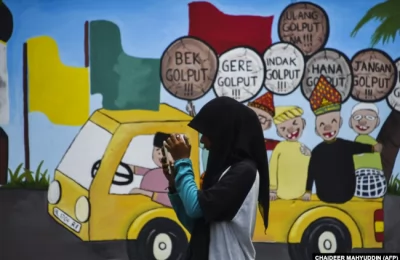 Seorang pemuda menggunakan ponselnya di depan mural kampanye Pemilu 2019, Banda Aceh, 17 Maret 2019. (Foto: AFP/CHAIDEER MAHYUDDIN)