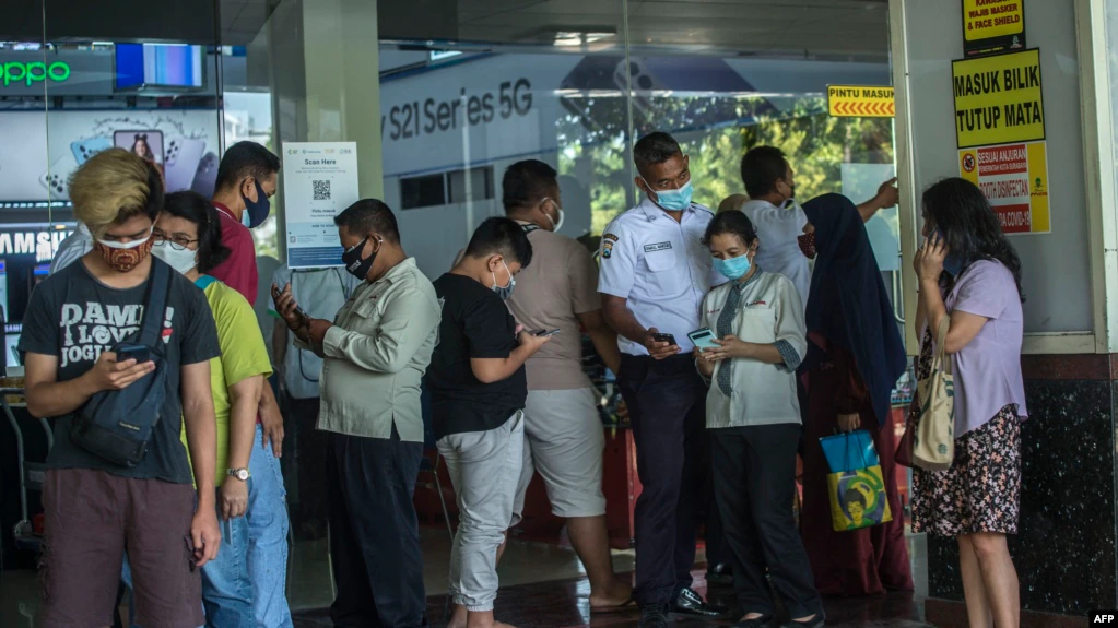 Orang-orang memindai kode QR untuk menunjukkan pelacakan kontrak tentang keberadaan mereka, sebelum memasuki pusat perbelanjaan di Surabaya pada 10 Agustus 2021, saat pemerintah menerapkan bentuk penguncian yang lebih ketat. (Foto: AFP/Juni Kriswanto)